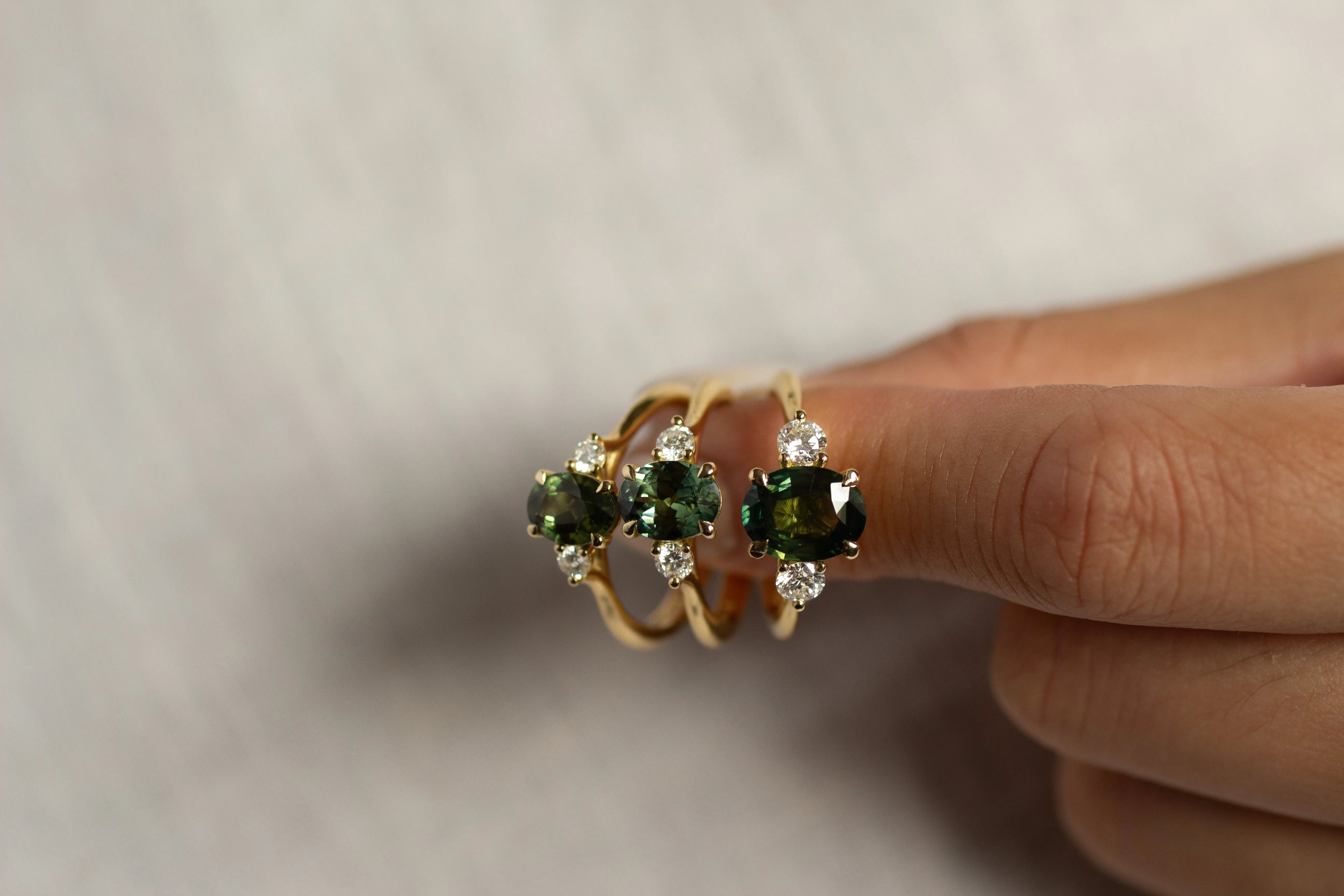 hands holding three green sapphire oval engagement rings with diamonds