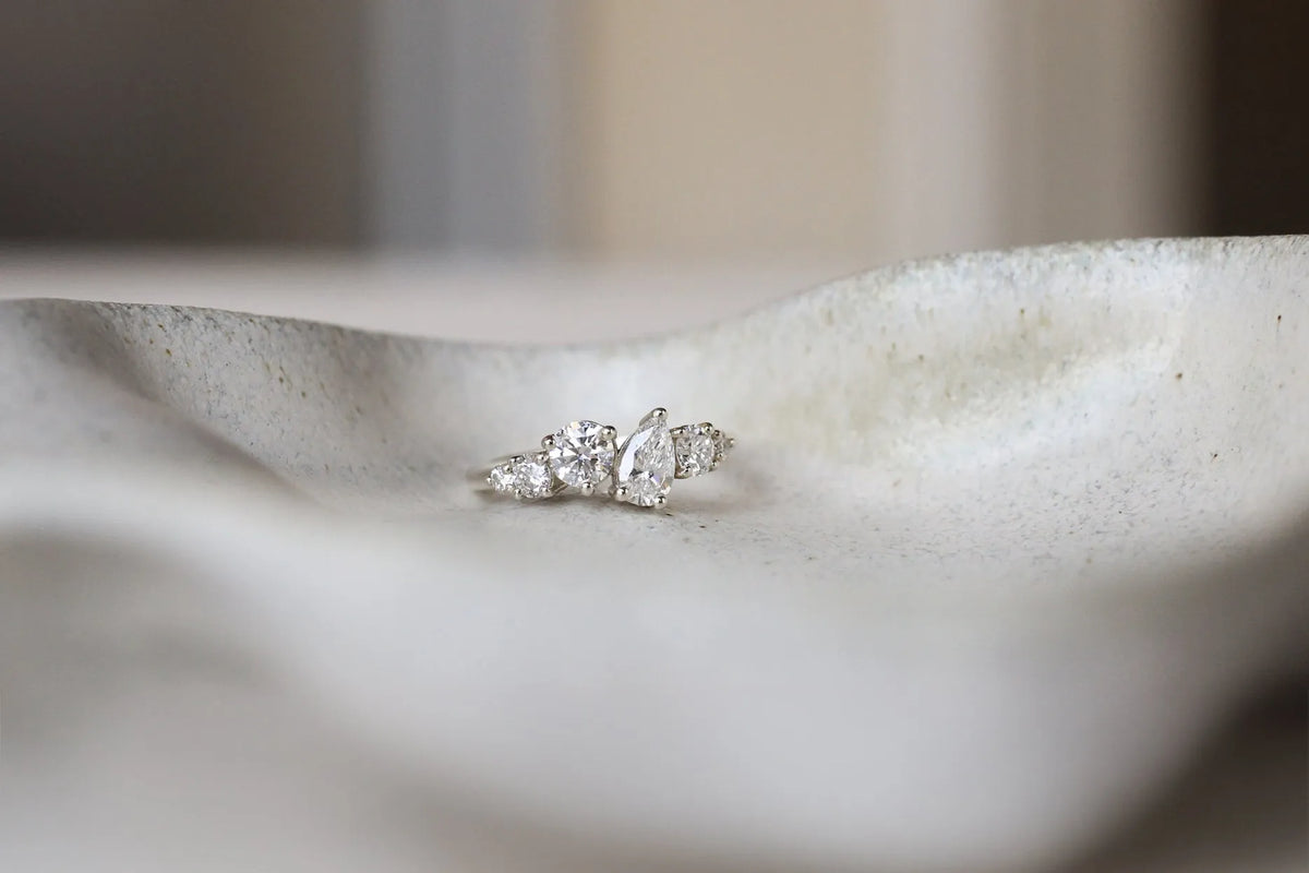 whie gold diamond asymmetric engagement ring with blurred foreground on a ceramic dish