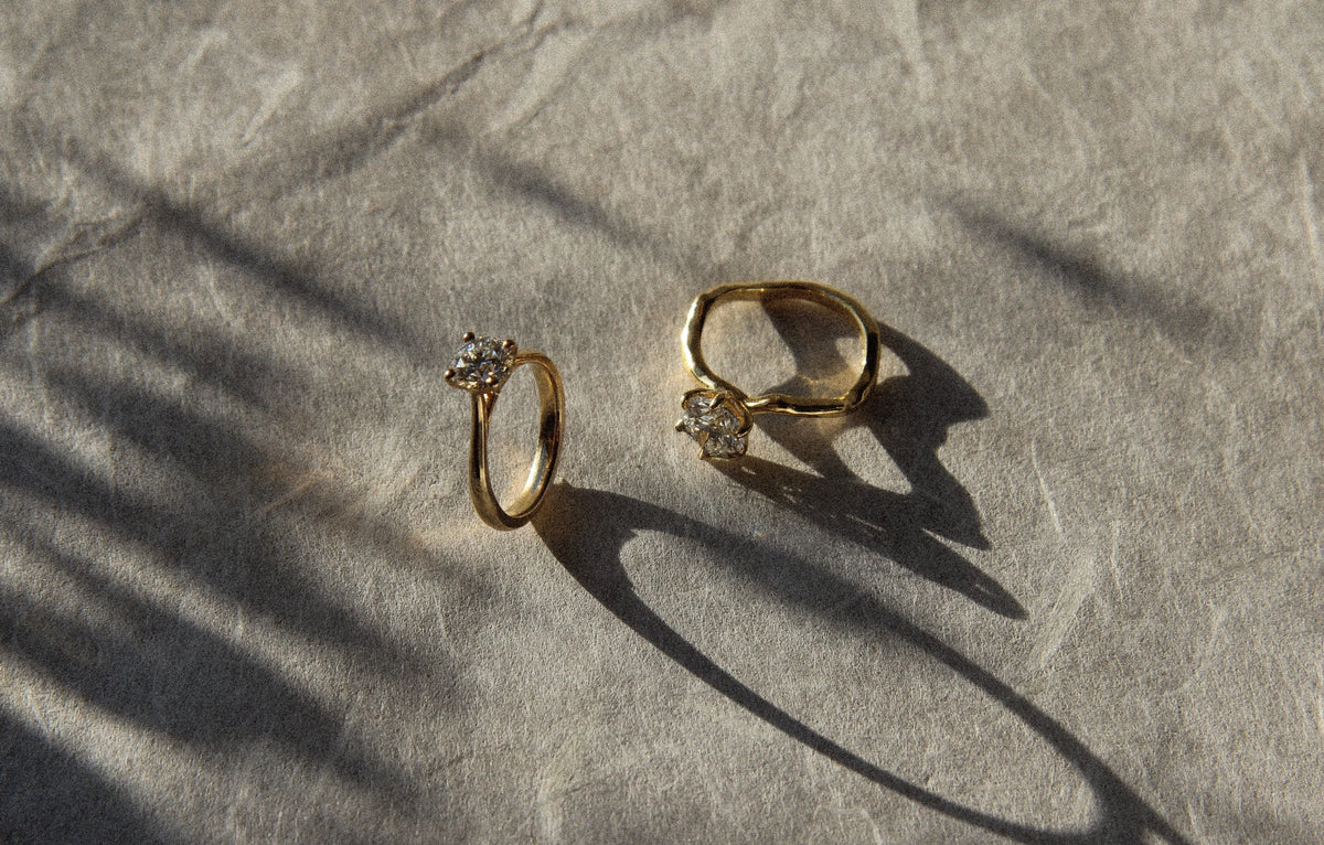 two diamond engagement rings on paper with shadows