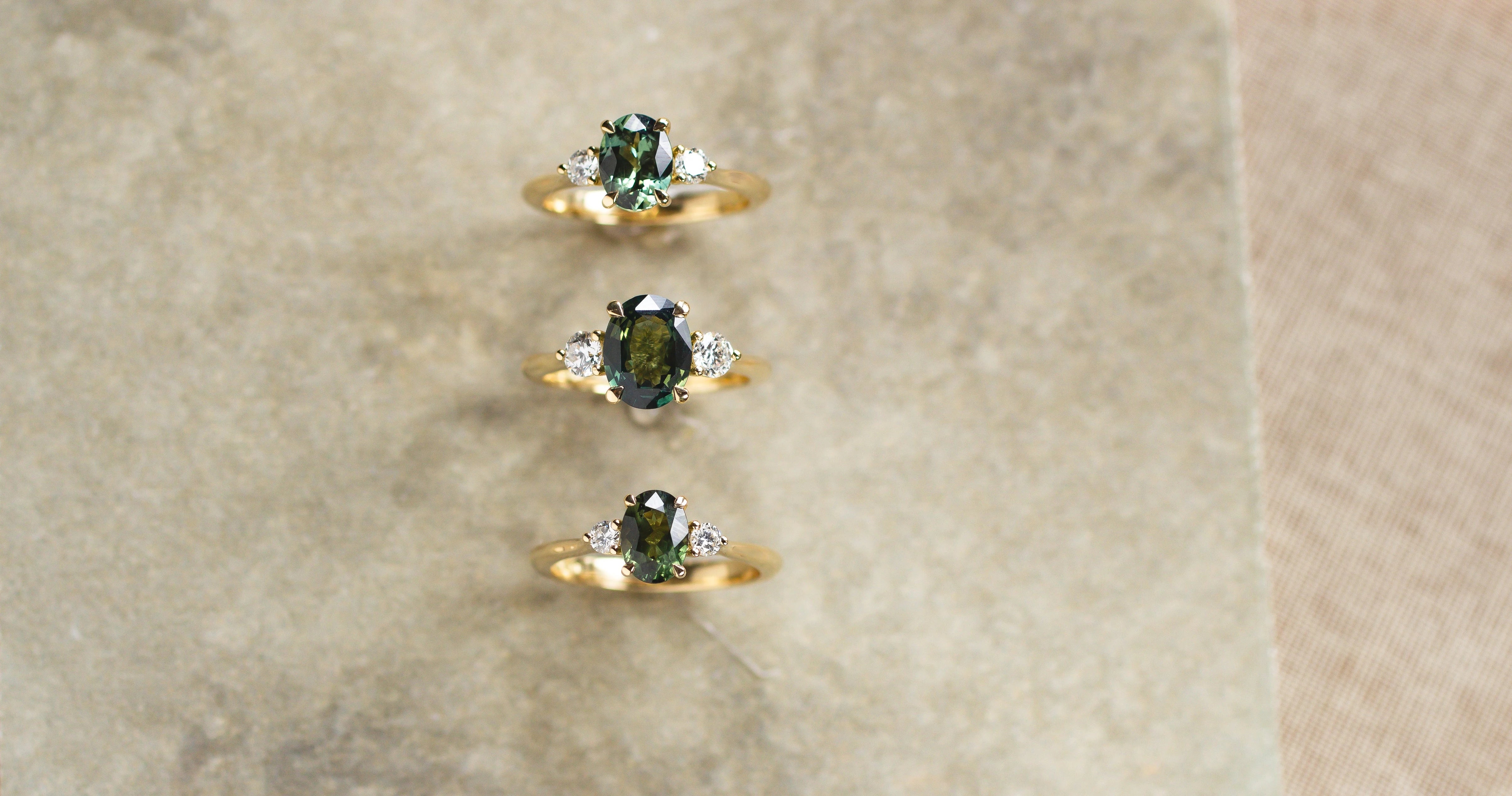 three trilogy engagement rings with green sapphires and diamonds