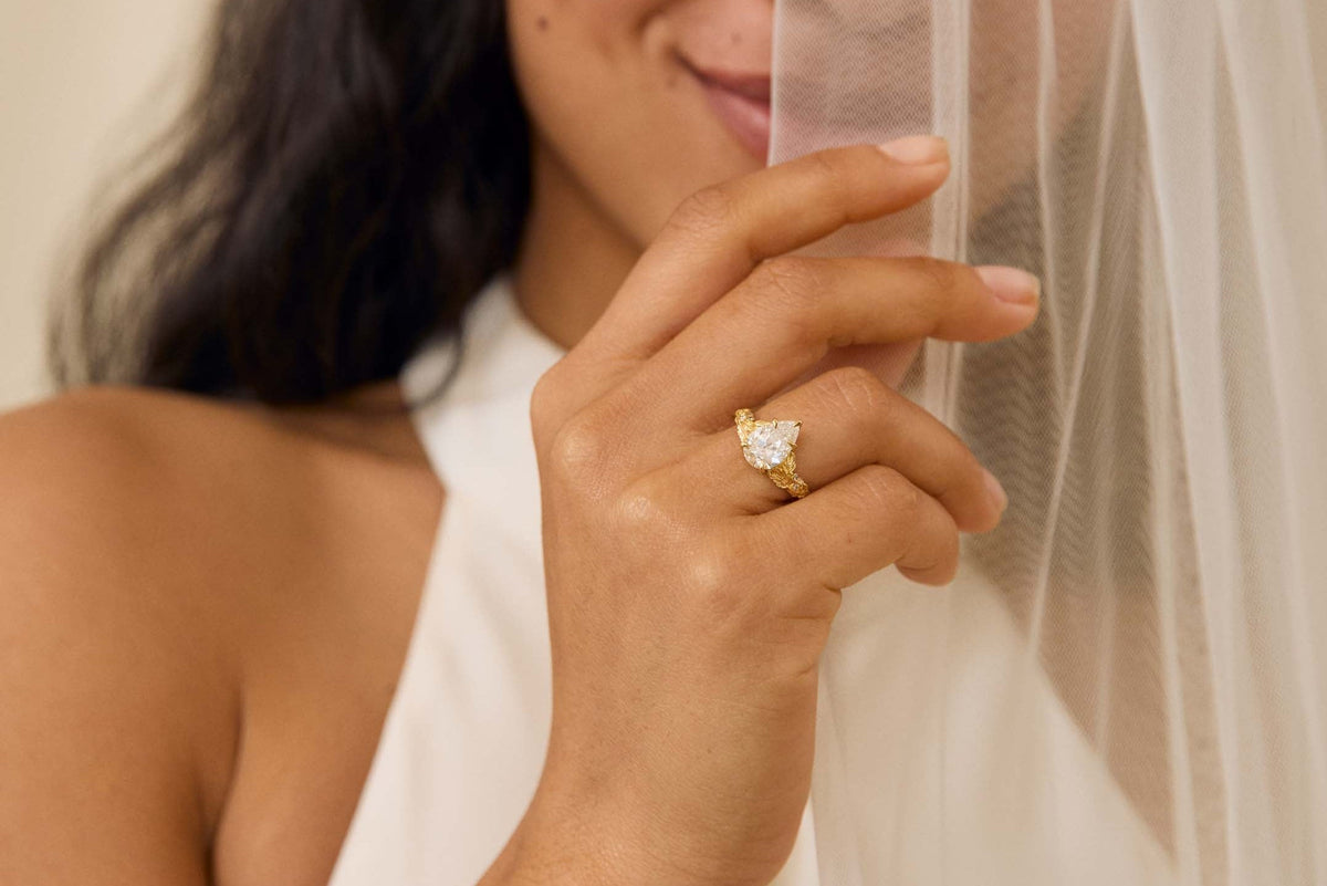 Woman holding a veil with a ring on her finger against a neutral background
