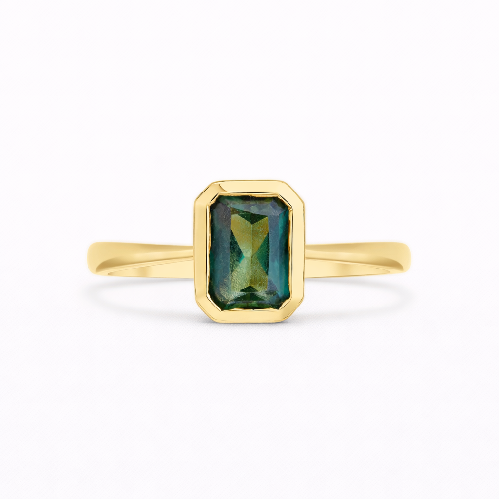 emerald cut sapphire solitaire engagement ring bezel set in gold on a white background