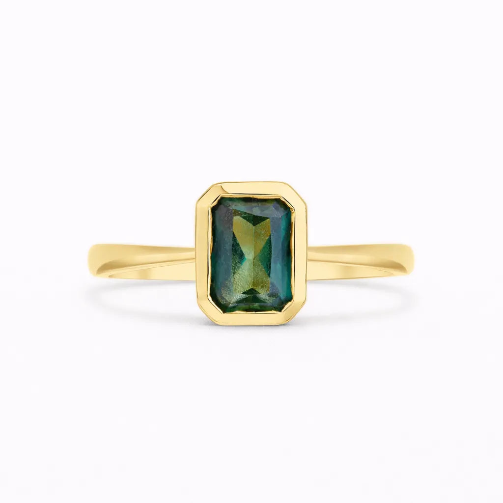 emerald cut sapphire solitaire engagement ring bezel set in gold on a white background