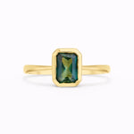 emerald cut sapphire solitaire engagement ring bezel set in gold on a white background