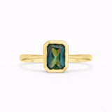 emerald cut sapphire solitaire engagement ring bezel set in gold on a white background