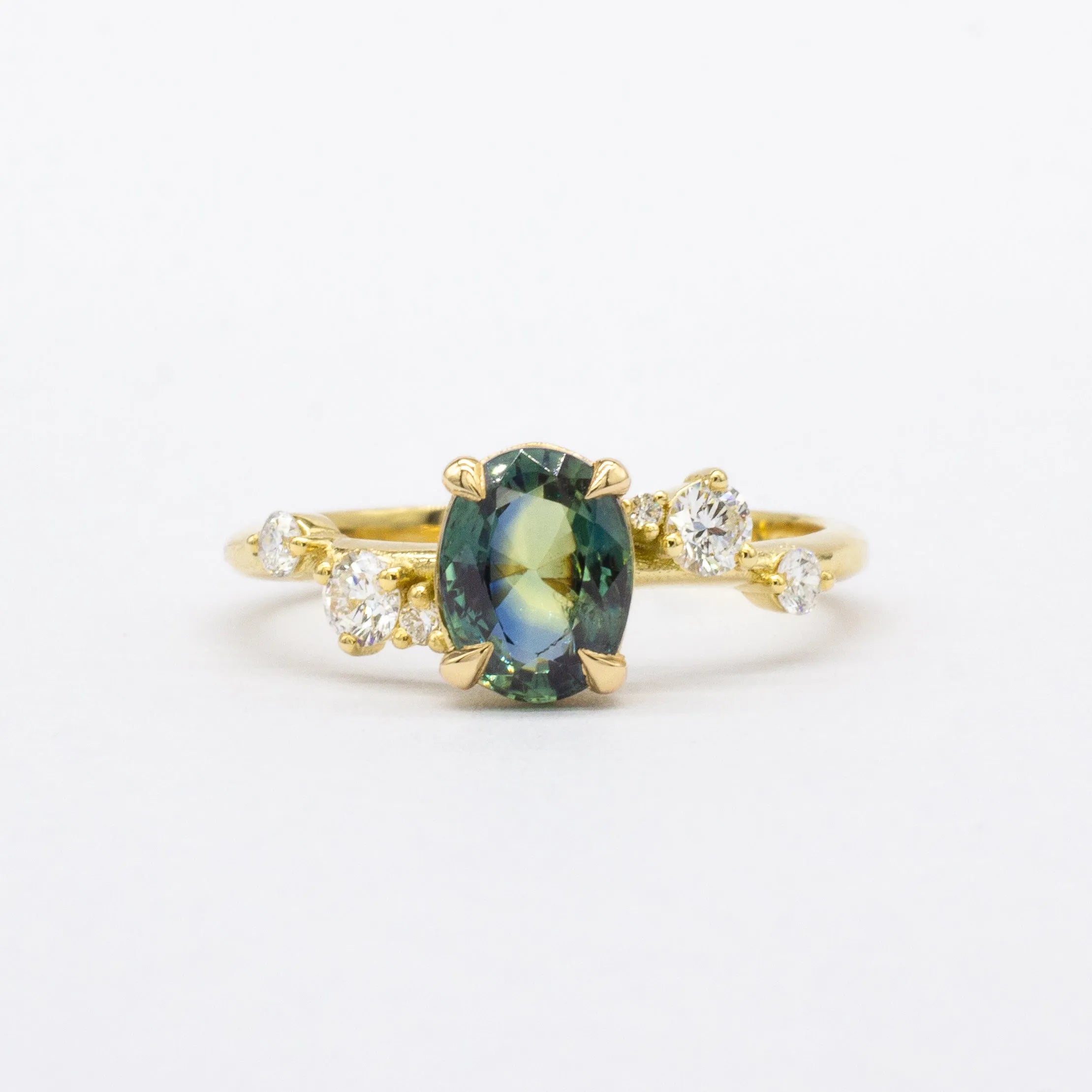 Gold ring with a green gemstone and diamond accents on a white background