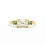 Gold ring with emerald-cut east-west diamond and green round sapphires on a white background