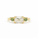 Gold ring with emerald-cut east-west diamond and green round sapphires on a white background