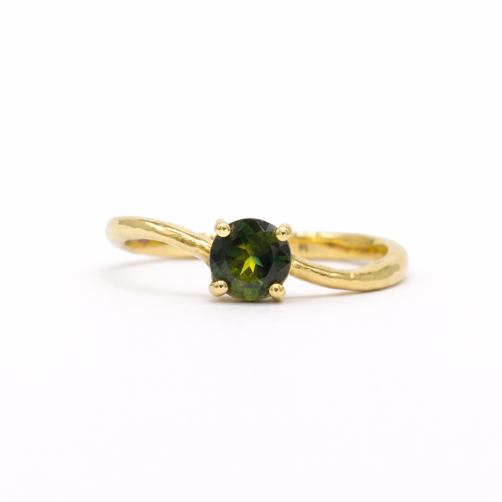 round green sapphire engagement ring with waved gold band on a white background