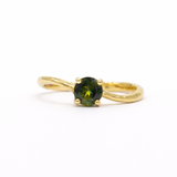round green sapphire engagement ring with waved gold band on a white background