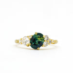 Gold ring with a green gemstone and diamond accents on a white background