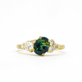 Gold ring with a green gemstone and diamond accents on a white background