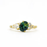 Gold ring with a green gemstone and diamond accents on a white background