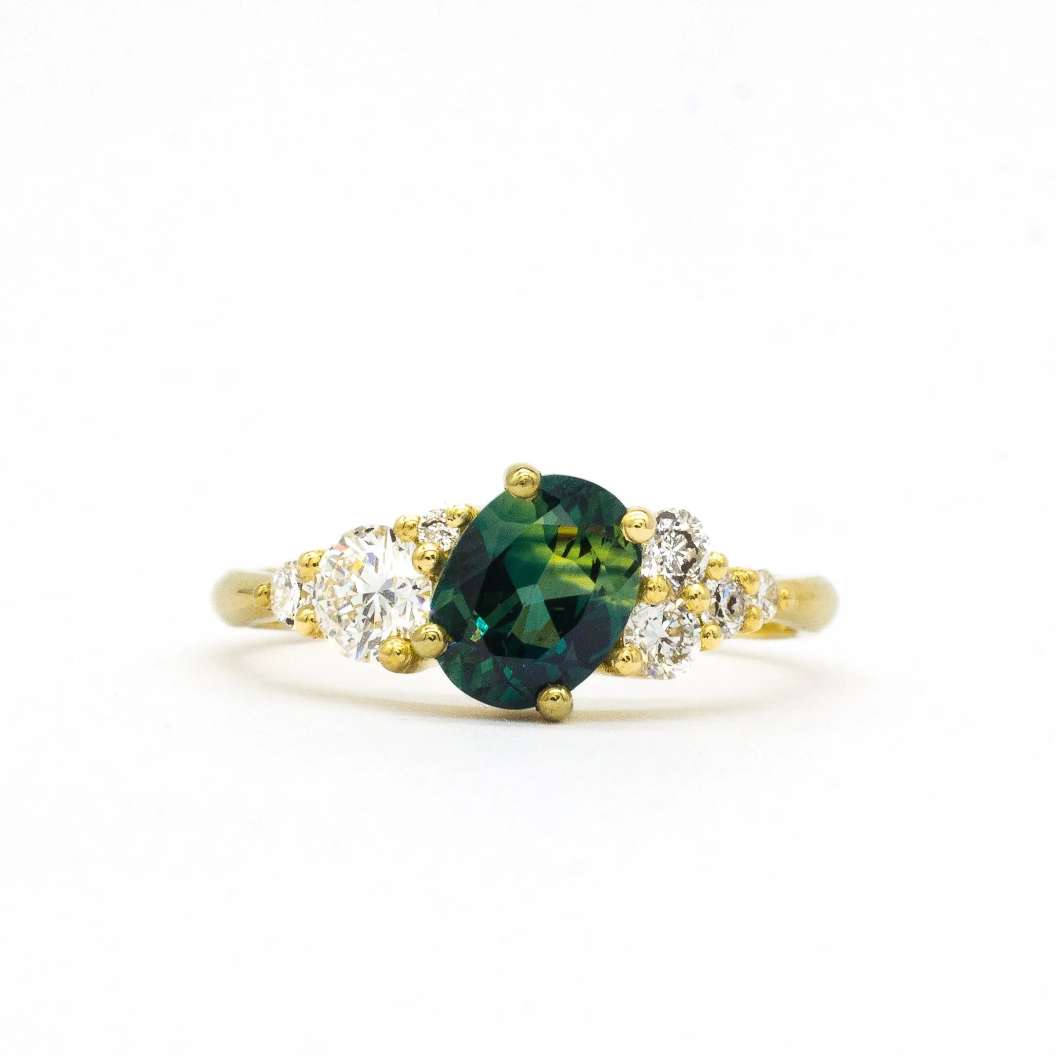 Gold ring with a green gemstone and diamond accents on a white background