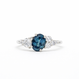 white gold engagement ring with a blue sapphire and diamond cluster on a white background
