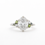 Diamond ring with green gemstones on a white background