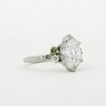 Diamond engagement ring with smaller green sapphires on a white background