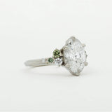 Diamond engagement ring with smaller green sapphires on a white background