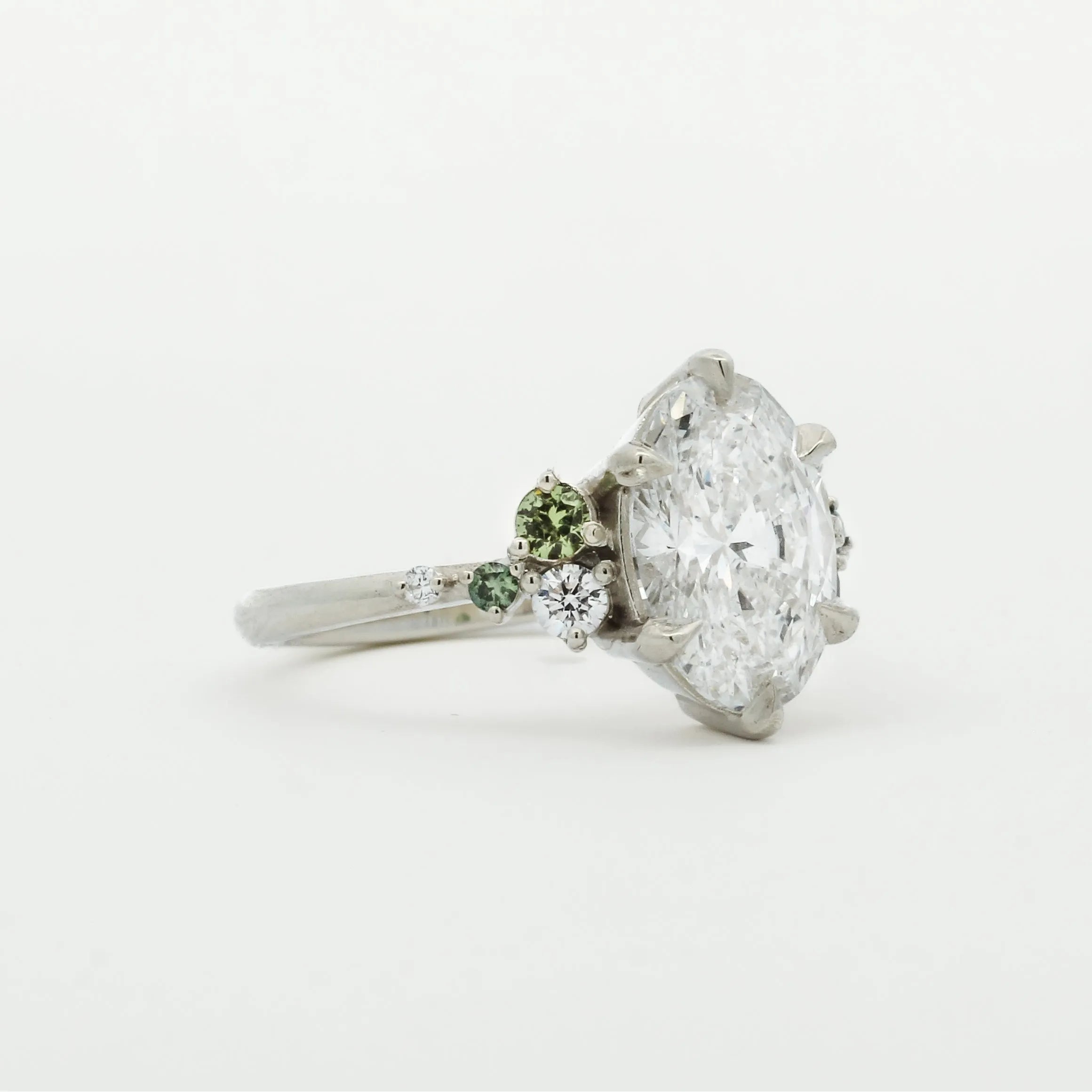 Diamond engagement ring with smaller green sapphires on a white background