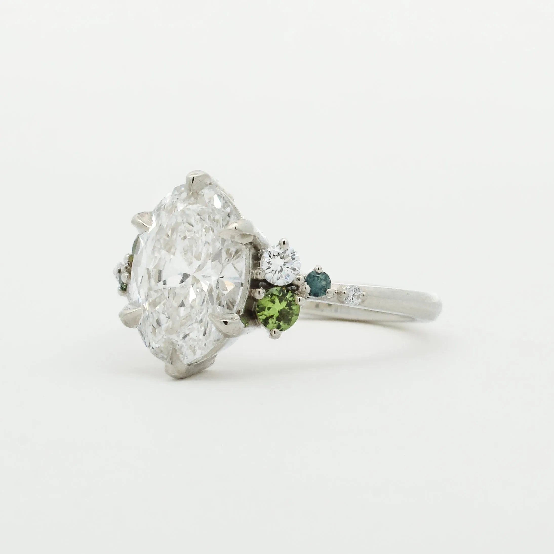 Diamond ring with green gemstones on a white background