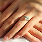 hand wearing large oval diamond engagement ring with smaller diamonds and blue and green sapphires, in the sunshine with shadows