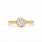 Gold ring with a round diamond bezel set with hammered hand on a white background