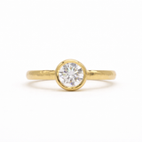 Gold ring with a round diamond bezel set with hammered hand on a white background