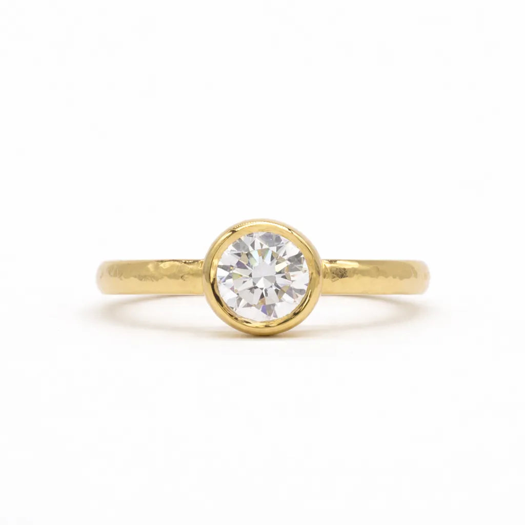 Gold ring with a round diamond bezel set with hammered hand on a white background