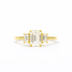 Gold ring with emerald-cut diamonds on a white background