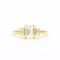 Gold ring with emerald-cut diamonds on a white background