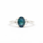 blue oval sapphire white gold engagement ring with round scattered diamonds on a white background