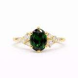 Gold ring with a green gemstone and leaf-like diamond accents on a white background