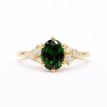 Gold ring with a green gemstone and leaf-like diamond accents on a white background