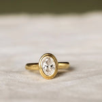 Double Bezel Set Solitaire Diamond Engagement Ring with oval diamond on a beige surface