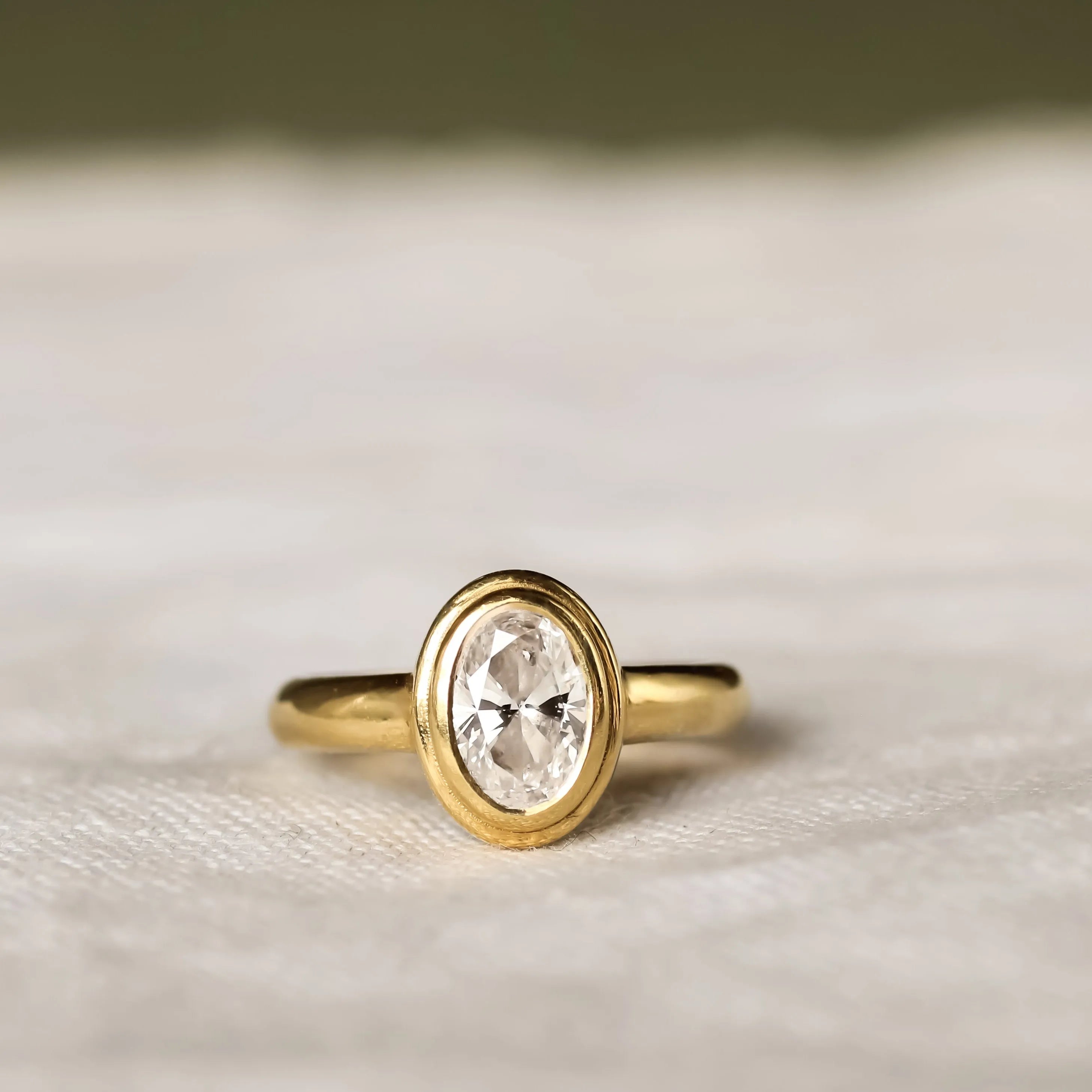 Double Bezel Set Solitaire Diamond Engagement Ring with oval diamond on a beige surface
