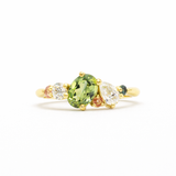 Gold ring with a green oval sapphire, pear diamond and pink and teal sapphires on a white background