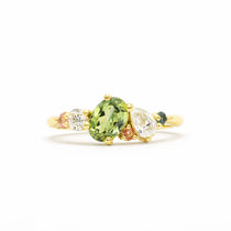 Gold ring with a green oval sapphire, pear diamond and pink and teal sapphires on a white background