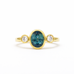 gold engagement ring with oval blue sapphire and round diamonds bezel set on a white background