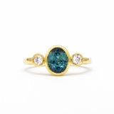 gold engagement ring with oval blue sapphire and round diamonds bezel set on a white background