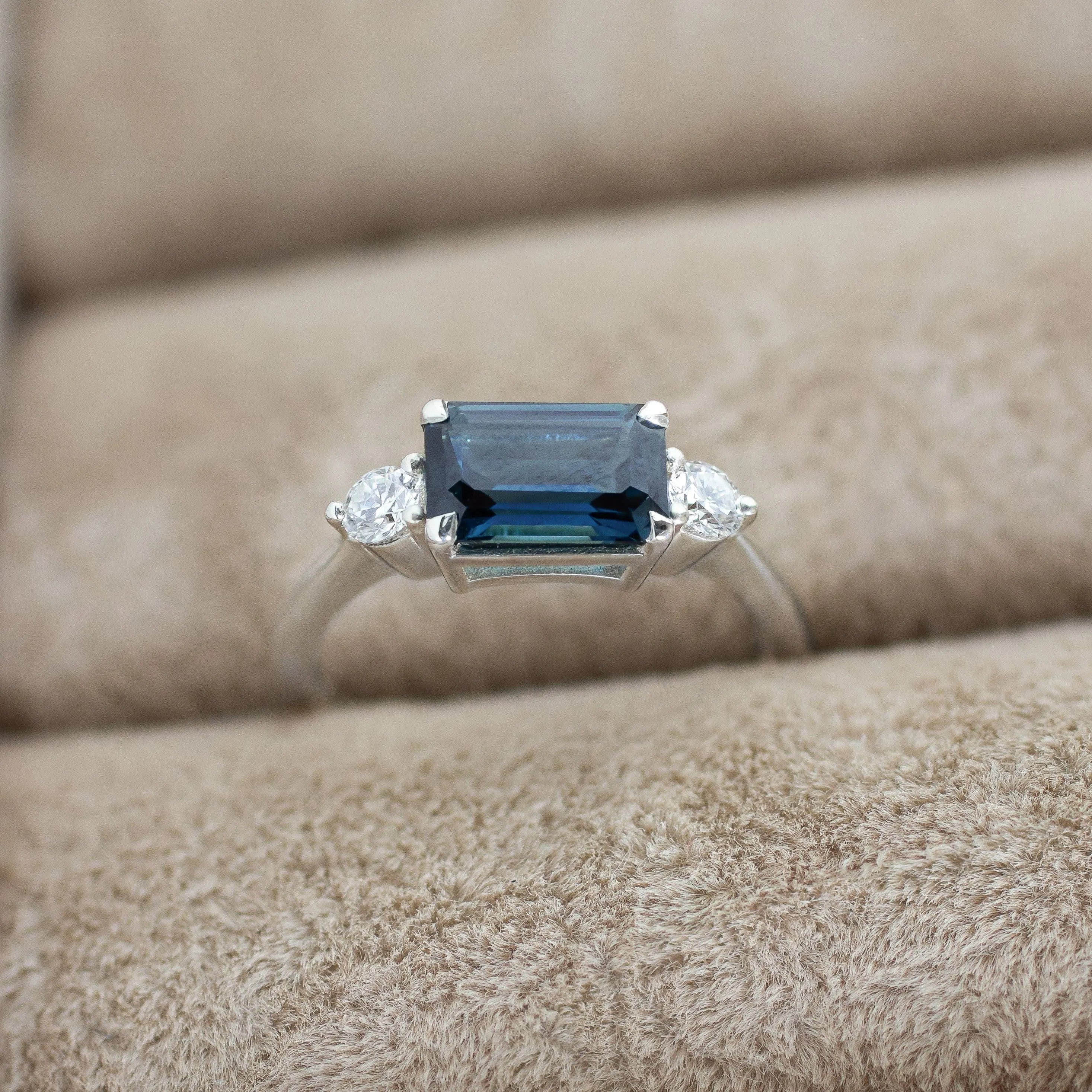 close up of white gold engagement ring with blue sapphire, round diamonds in ring box slot