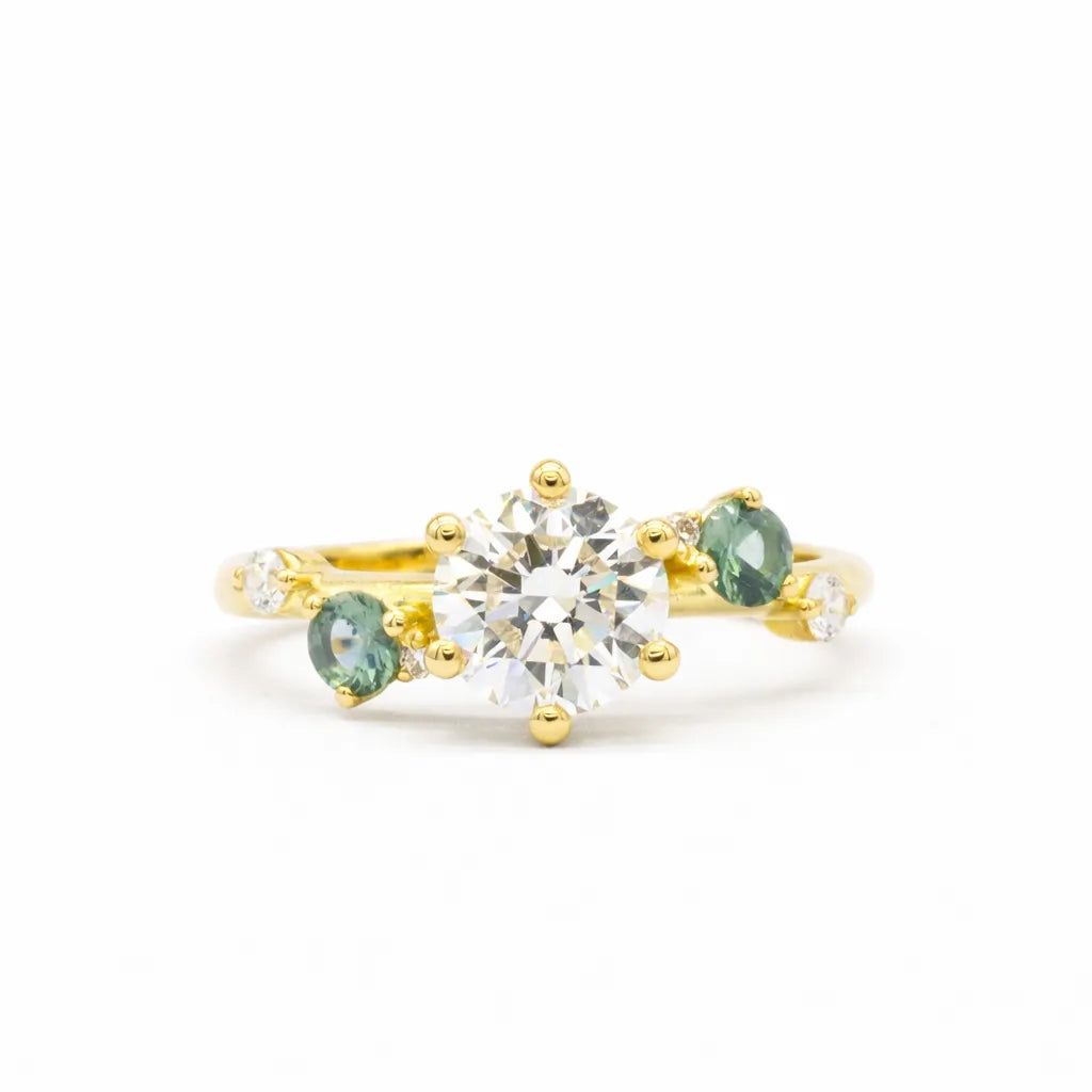 Gold ring with central diamond and green gemstones on a white background