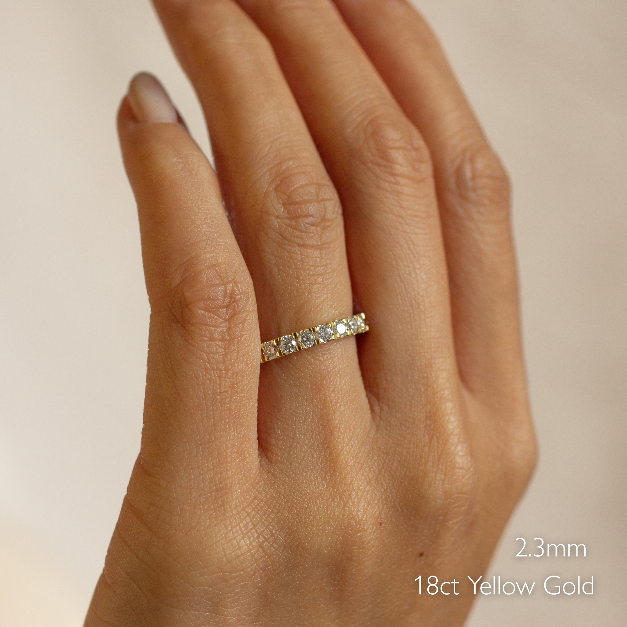 Hand wearing a diamond ring with '2.3mm' and '18ct Yellow Gold' text on a neutral background