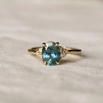 teal sapphire engagement ring with diamond cluster and blurred background