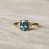 teal sapphire engagement ring with diamond cluster and blurred background