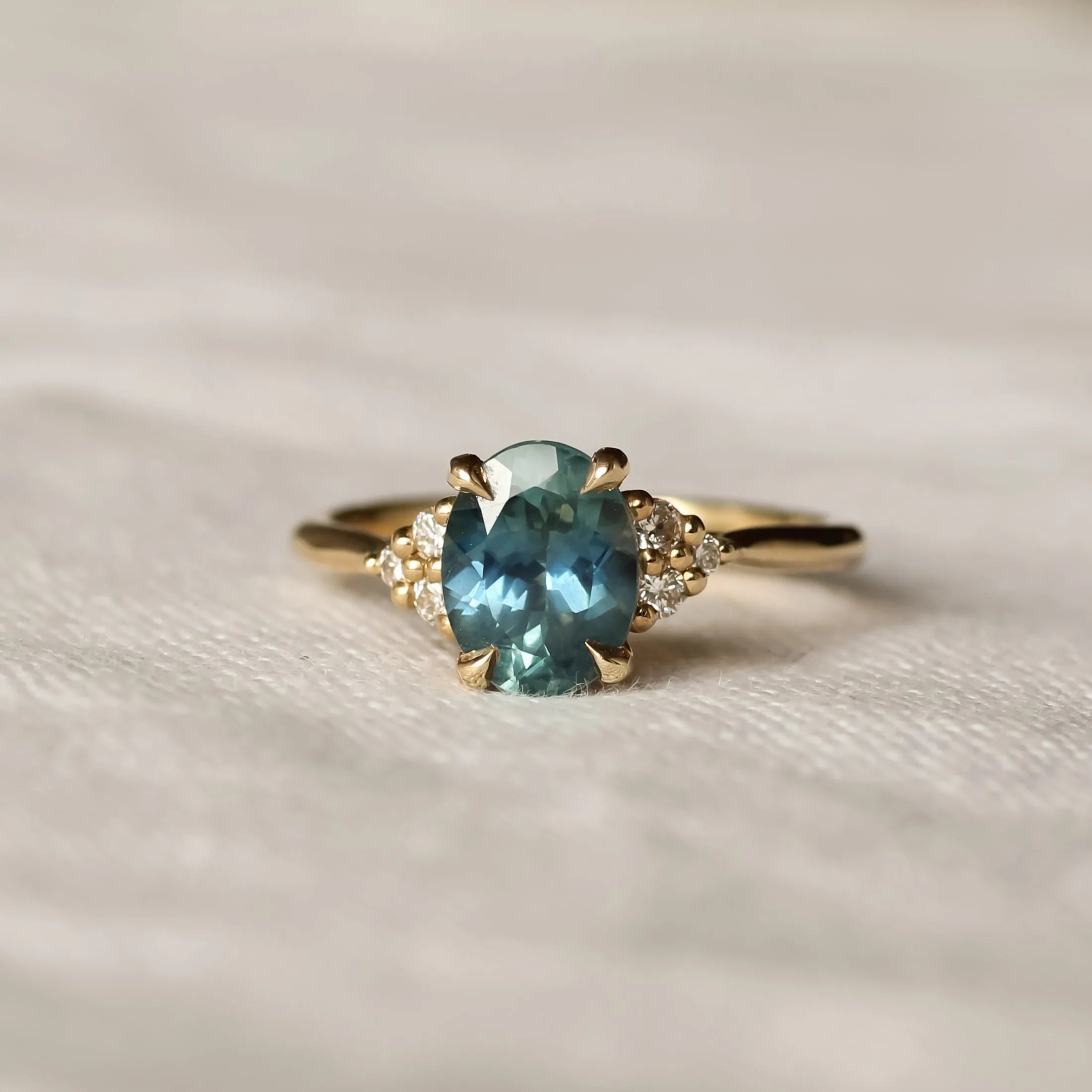 teal sapphire engagement ring with diamond cluster and blurred background