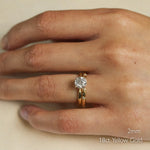 Hand wearing a 2mm wedding gold ring with a diamond engagement ring on a beige background