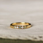 gold ring with 5 gemstones including diamonds and blue green sapphires on a beige fabric