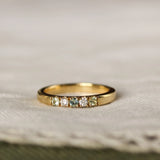 gold ring with 5 gemstones including diamonds and blue green sapphires on a beige fabric