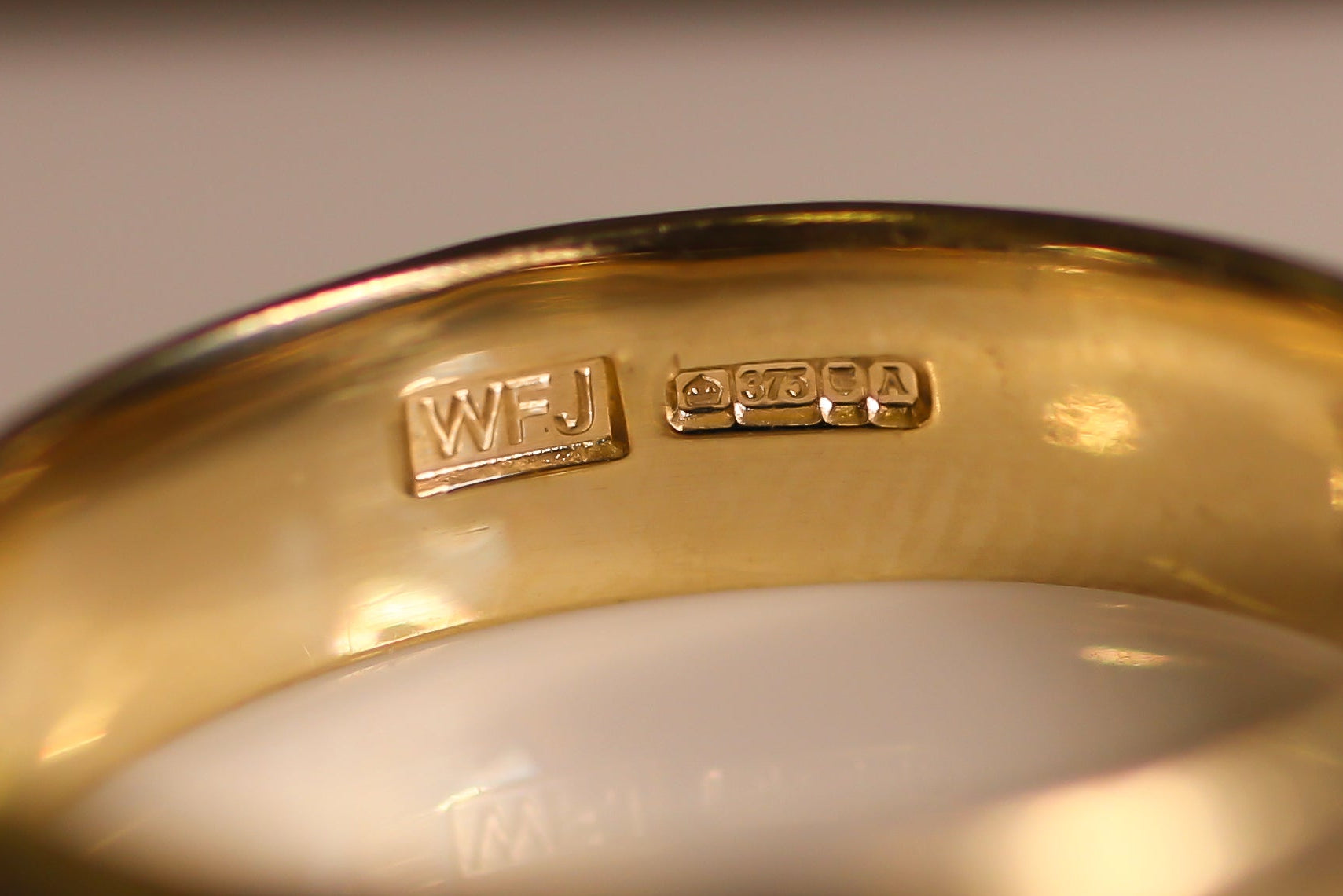 Gold ring with visible hallmark 'WFJ', crown symbol, '375', anchor and 'A' on a light background
