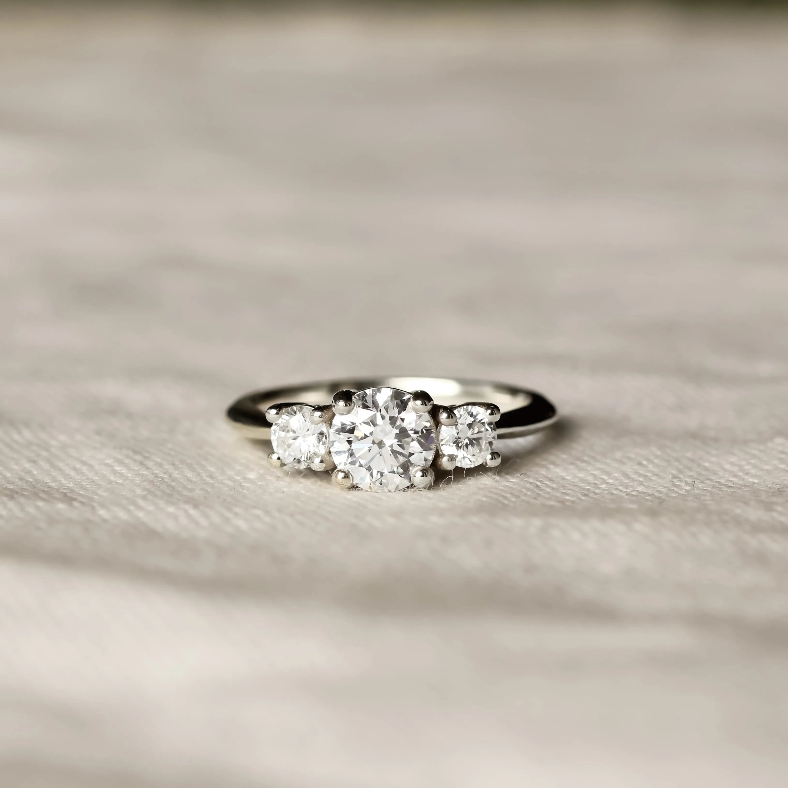 Trilogy Diamond White Gold Engagement Ring with three diamonds on a beige fabric surface